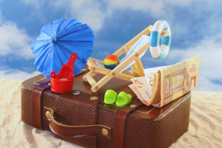 Valise de vacances avec accessoires de plage et argent symbolisant les congés payés.