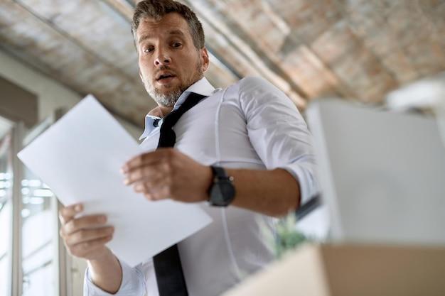 Vue en contre-plongée d’un homme d’affaires lisant un avis de licenciement au bureau